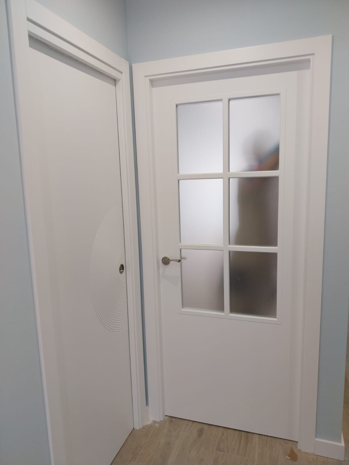 Puerta de paso blanca de seis luces con zócalo, junto a otra puerta lacada en blanco